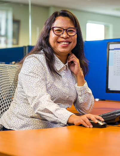 A woman sat at a desk on a computer smiling towards the camera