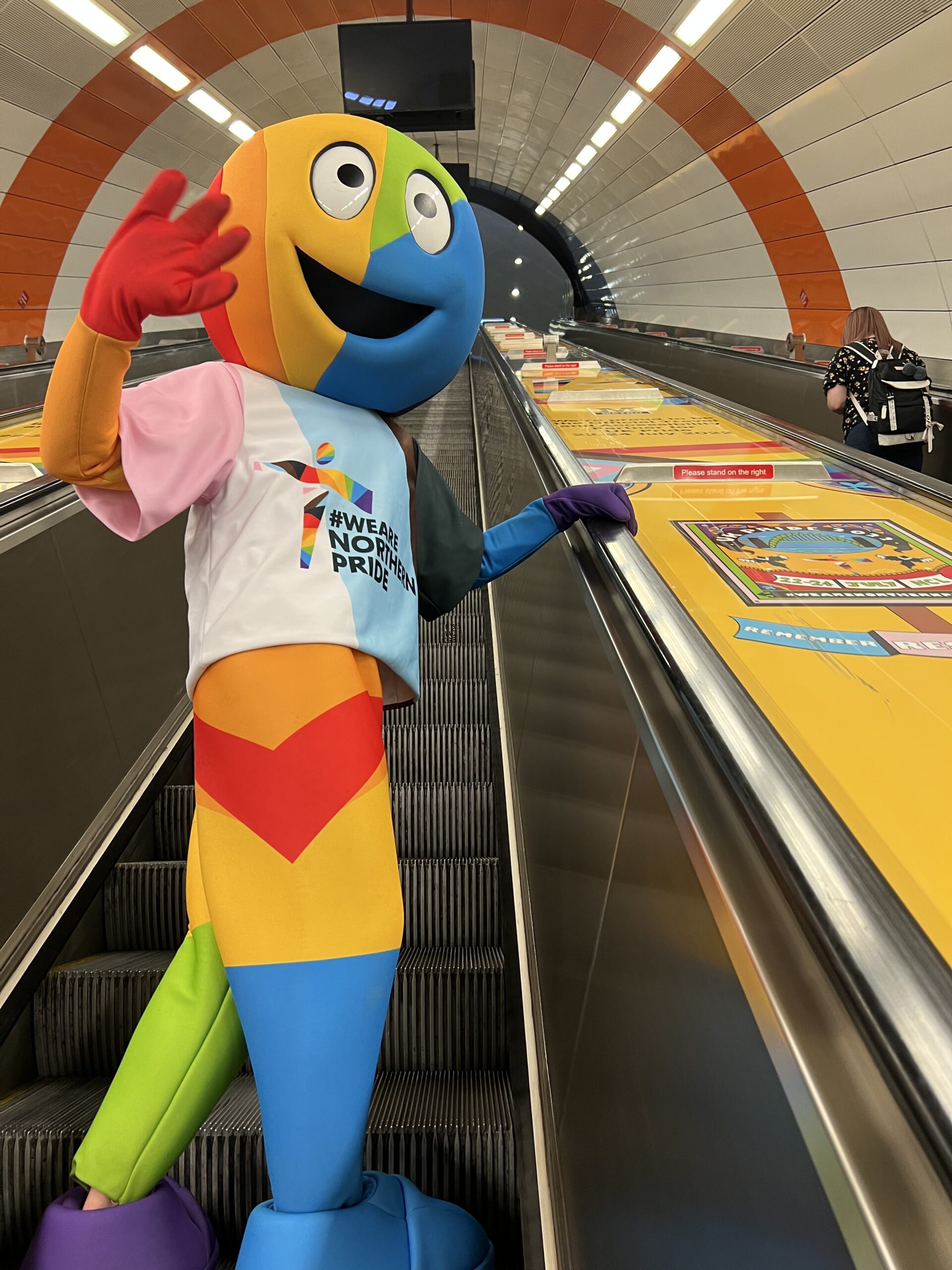 A brightly coloured Pride mascot on an escalator at Haymarket metro station