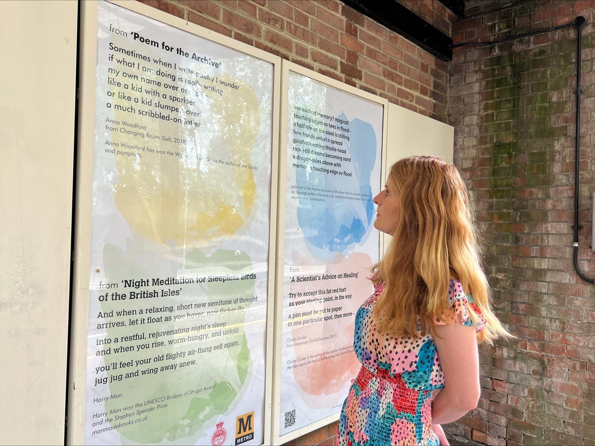 An image of a woman looking at a display of poetry on a wall at a Metro station