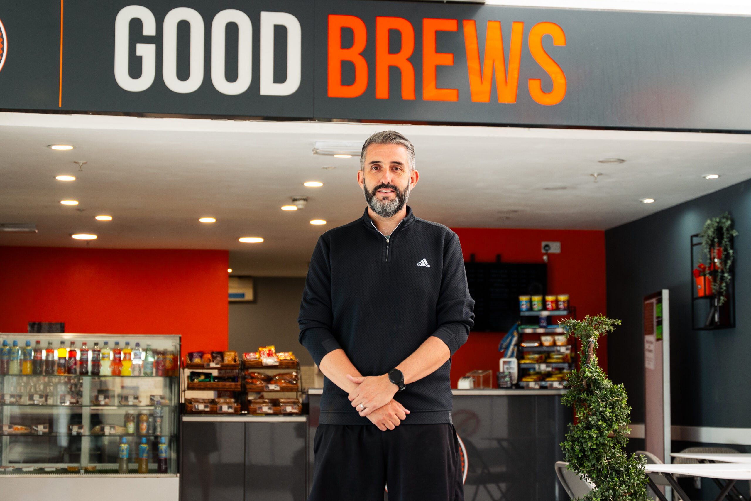 A photo of a man standing outside a coffee shop with a sign saying Good Brews