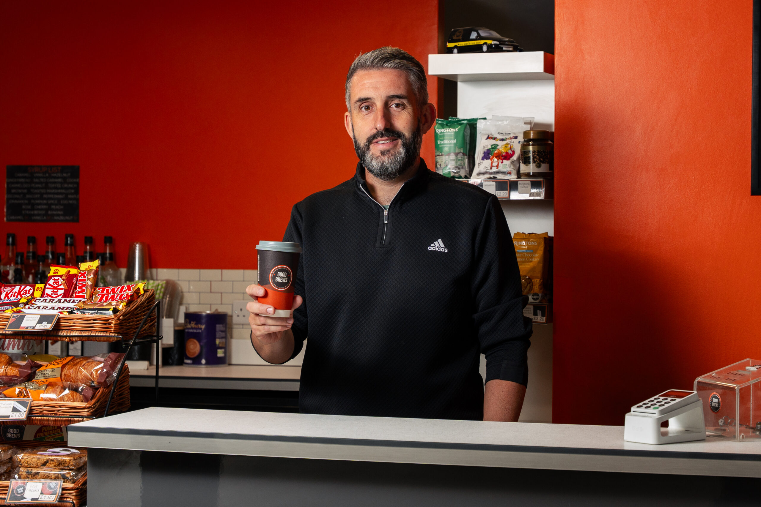 A picture of a man holding a cup of coffee behind the counter in a coffee shop